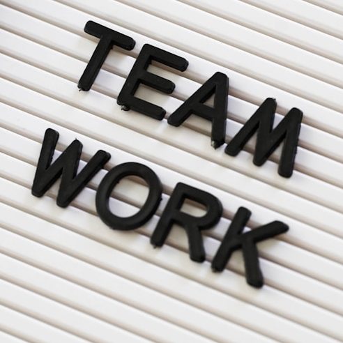 Schwarze Buchstaben formen die Wörter "TEAM" und "WORK" auf einem hellem Untergrund.